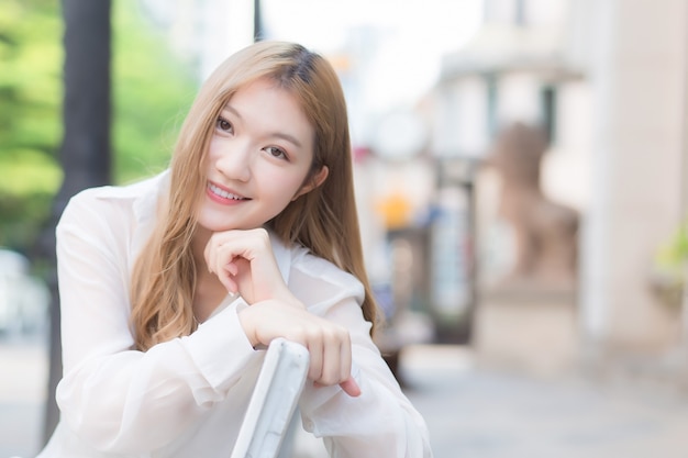 Asian beautiful girl with bronze hair in white shirt while sits happy smilie on the edge