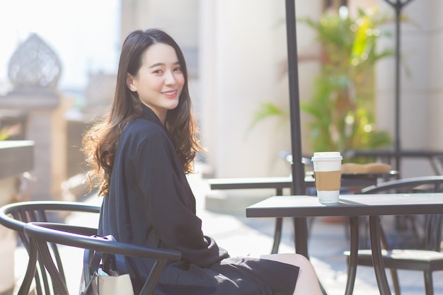 Asian beautiful lady in a dark blue suit is sitting on a chair and smiling happily