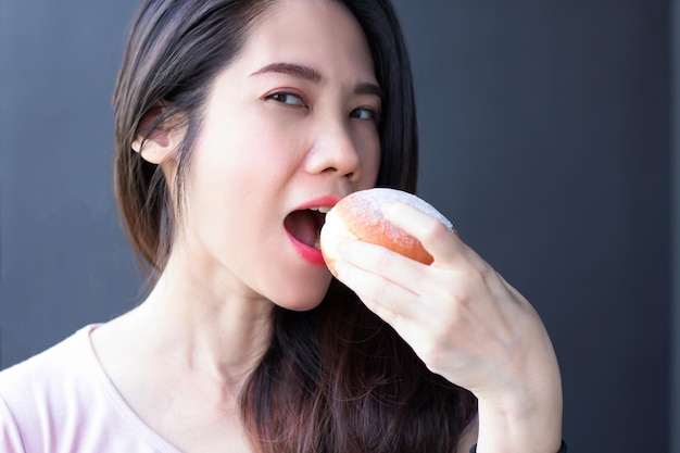 아시아의 아름다운 여성이 커피 브레이크나 아침 식사 중에 웃고 행복하며 도넛 빵을 먹고 있습니다