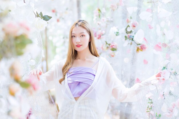 Asian beautiful woman blonde wearing purple shirt while smiles and stands in rose flower garden.