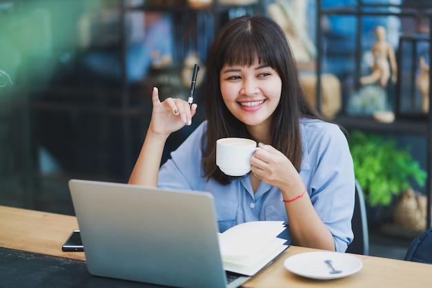 Asian beautiful woman  in blue shirt  using laptop and drinking coffee