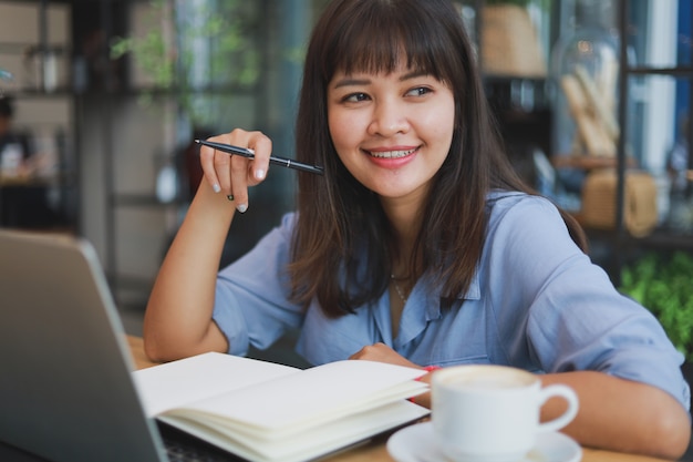 Asian beautiful woman  in blue shirt  using laptop and drinking coffee