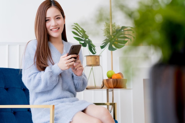 Asian beautiful woman enjoy morning weekend with hand smartphone and hot drink on chair bedroom background