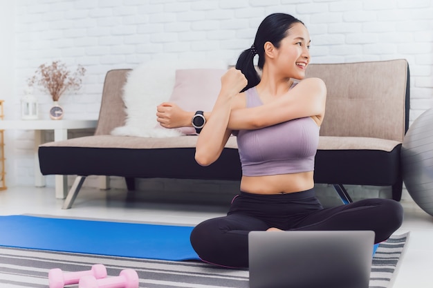 Азиатская красивая женщина упражнения дома и просмотр обучающего видео на ноутбуке.