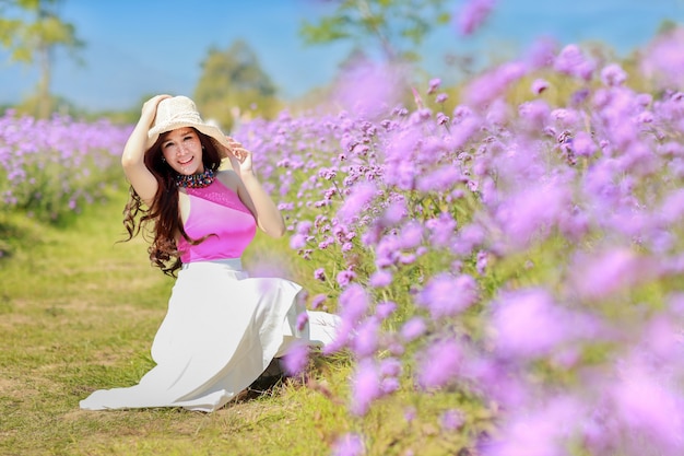 Asian beautiful woman, long hair in cute dress on Verbena with blue sky. Beautiful cute girl portrait enjoying flowers in flowers farm background. Travel in nature outdoor concept