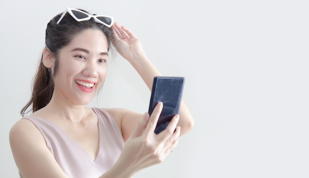 Asian beautiful woman looking on smartphone and raise hand touch on sun glasses and smile with happiness during chatting or shopping online or win a lottery or win game