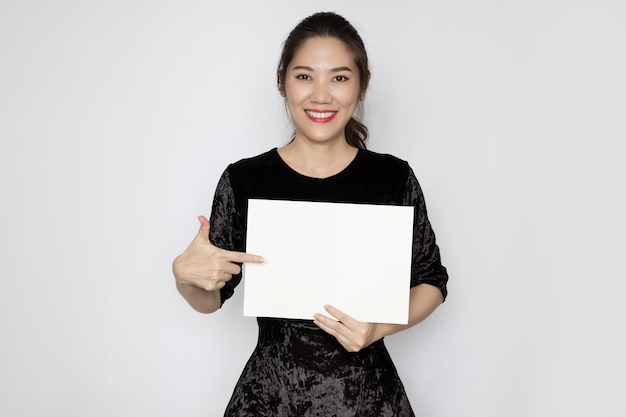 Asian beautiful woman makes pointing gesture hand sign and holding white paper or board for writing text or an information to communicate to people