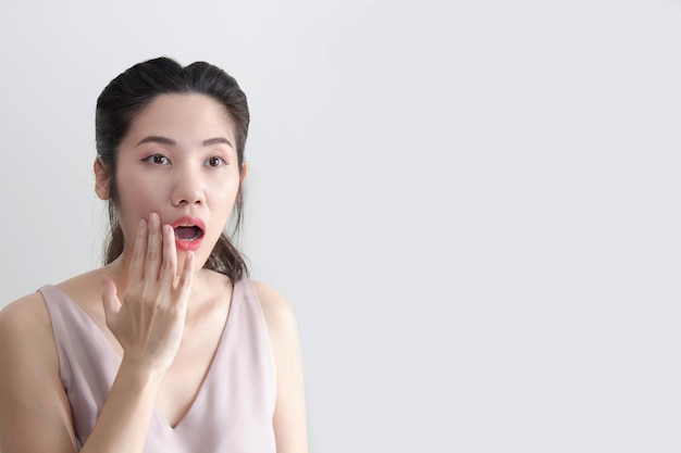 Asian beautiful woman raise hand touching her lips and open mouth and looking away with shocking and surprising