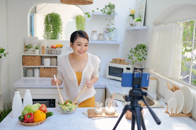 휴대 전화를 사용하여 요리 비디오를 녹화하는 아시아의 아름다운 여성.