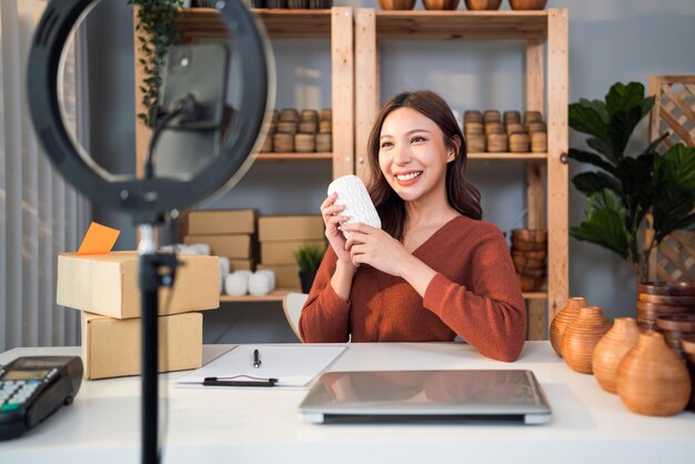 Foto bella donna asiatica vende prodotti in vaso online in diretta streaming a casa giovane ragazza attraente