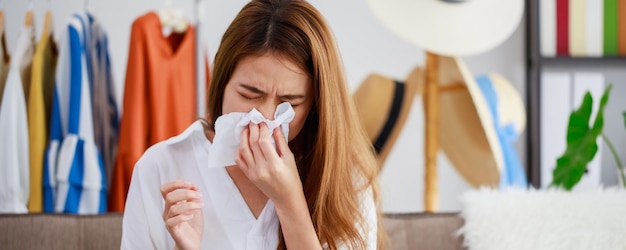 Asian beautiful woman sick with the flu and fever while working with a laptopHand holding tissue paper after taking a cold medicationConcept of hard work without maintaining health