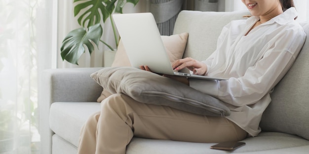 asian beautiful woman sit on sofa and use laptop for chat at home happy attractive young girl spend leisure time at home feel relax and enjoy communicate and discuss on laptop in living room