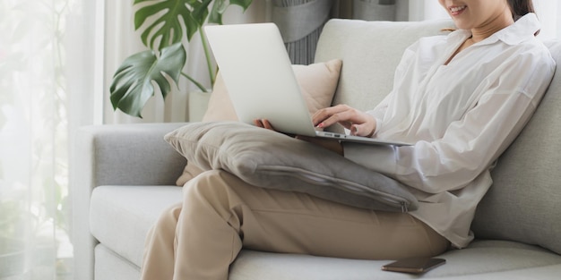 Asian beautiful woman sit on sofa and use laptop for chat at\
home happy attractive young girl spend leisure time at home feel\
relax and enjoy communicate and discuss on laptop in living\
room