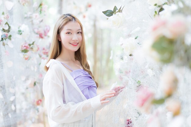 La bella donna asiatica che indossa una camicia bianca e viola sorride e si trova in un giardino fiorito di rose bianche