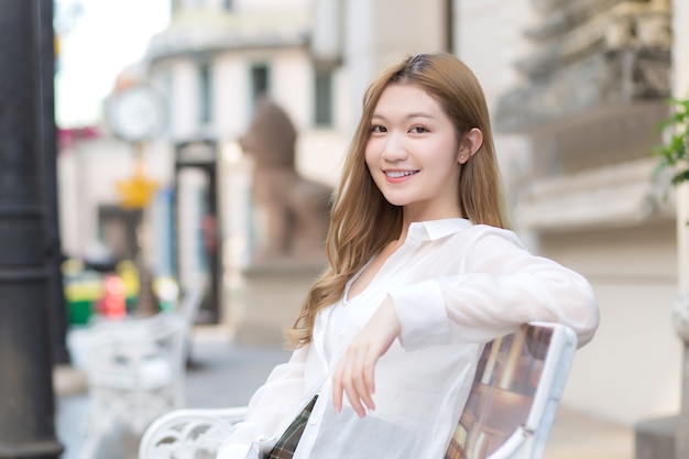 Asian beautiful woman with bronze hair  in white shirt while sits happy smilie on the edge of a city