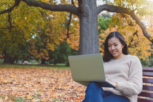 Asian beautiful woman working with laptop while sitting in garden with falling leaf