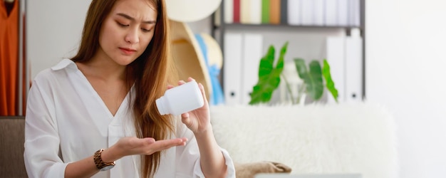 Belle donne asiatiche stressanti e mal di testa dopo aver lavorato a lungo con un computer portatile mano che tiene una bottiglia di medicina del mal di testa concetto di sindrome da ufficio