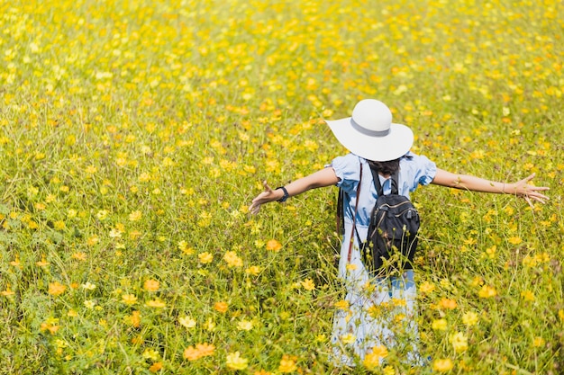 写真 歩いて、黄色いコスモスの花畑の風景の背景で写真を撮るアジアの美しい若い女性タイで夏の季節の旅行のコンセプト