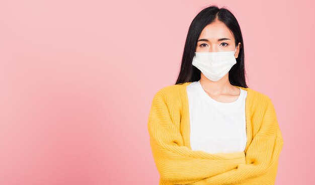 감염 코로나바이러스를 예방하기 위해 의료용 마스크를 착용한 아시아의 아름다운 젊은 여성, COVID-19 그녀는 팔짱을 끼고 분홍색 배경 복사 공간 의료 개념에 격리된 스튜디오 샷