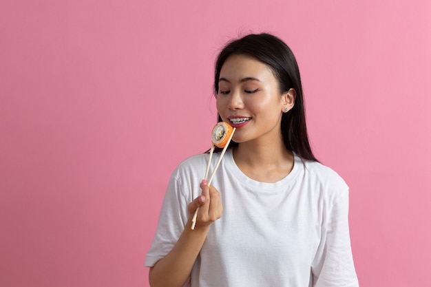 Asian beauty model girl going to eat Sushi roll, healthy japanese food. Beautiful woman holding chopsticks with Philadelfia roll.