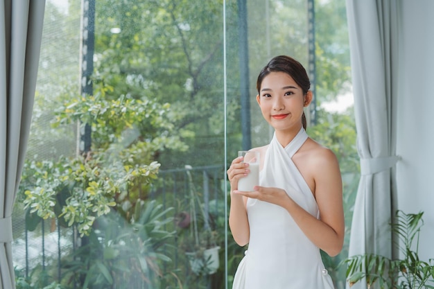 コピースペースで朝の窓の近くに立ってミルクのガラスを保持しているアジアの美女の友人