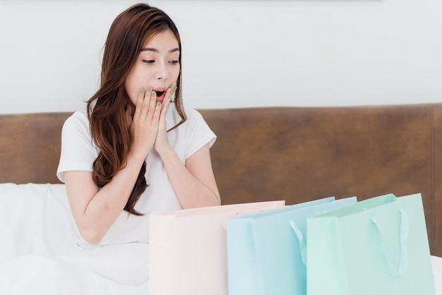 Азиатская красавица удивлена сумками для покупок Со счастливым улыбающимся лицом, будучи новым нормальным онлайн-бизнесом. В процессе покупок из дома.