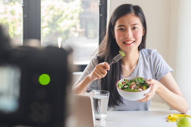 Foto blogger asiatico che mangia insalata e registra video