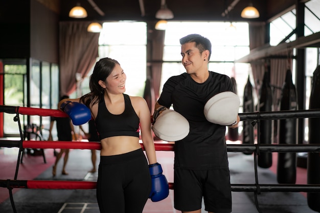 Asian boxer sports girl and trainer looking  smile while leaned on black red ropes on boxing ring