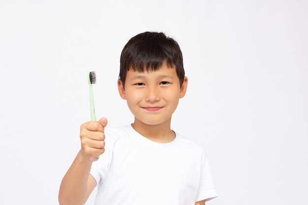 Asian boy brushing teeth, isolated on white surface