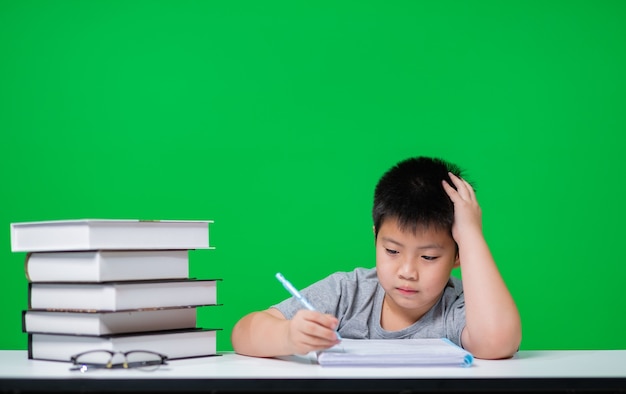 Asian boy doing homework on green screen, child writing paper,  education concept, back to school