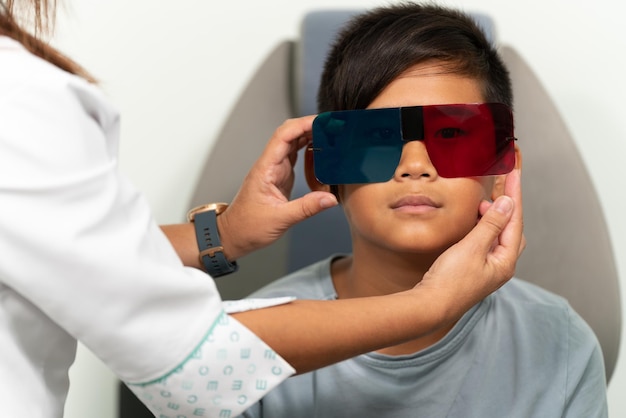 Asian boy in a duochrome test review with red and green 3D glasses The optometrist is putting a glasses on him