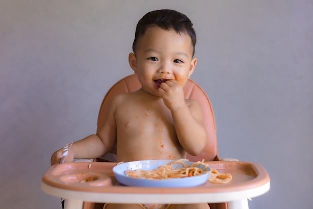 高い赤ん坊の椅子で食べるアジアの少年。