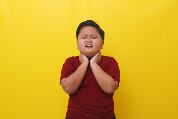 Asian boy feels uncomfortable with his neck healthcare concept\
isolated on yellow background