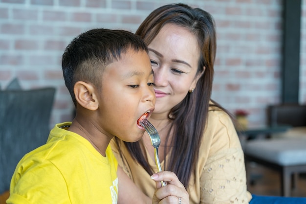 Asian boy  is eating the food from his mother