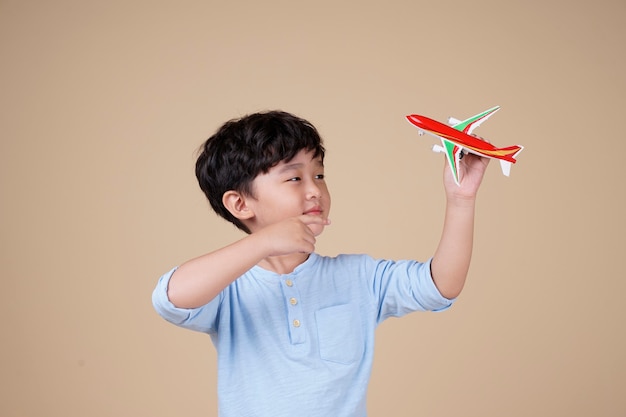 アジアの少年はベージュで隔離の飛行機のおもちゃで旅行するのが楽しみです
