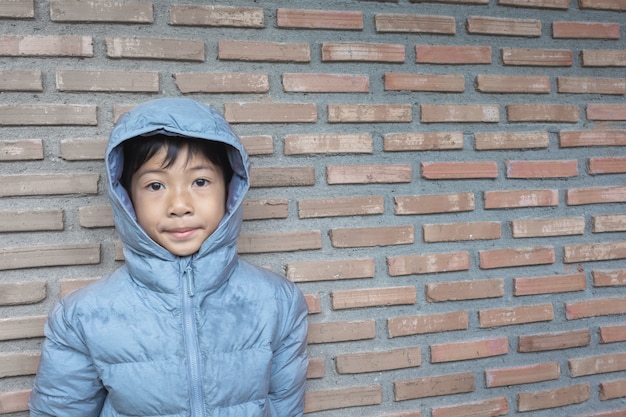 Asian boy is wearing a hood on brick wall background