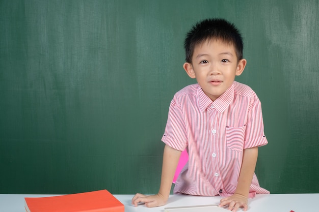 アジアの男の子は、チョークボードルームで探しています。学校への教育コンセプト