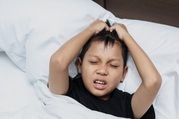 Азиатский мальчик, лежащий на кровати, страдает головной болью
