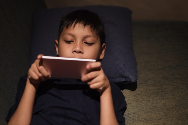 Asian boy lying and playing game on smartphone