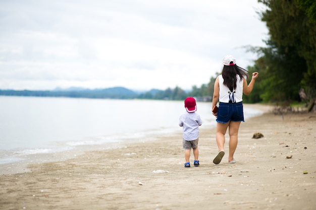 Asian boy and mother walking the tropical beach, Happy little boy walking near the sea