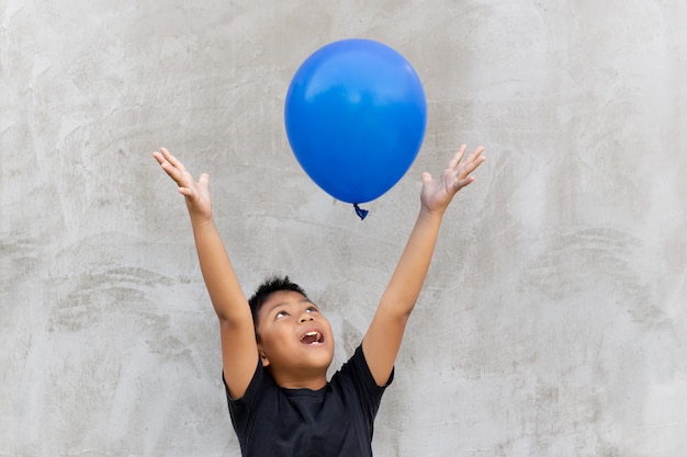 Asian boy play catches balloon on grey background.