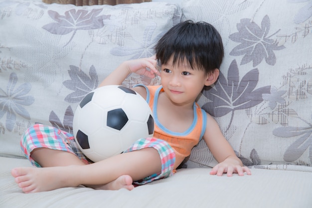 Asian boy play football on the sofa in living room