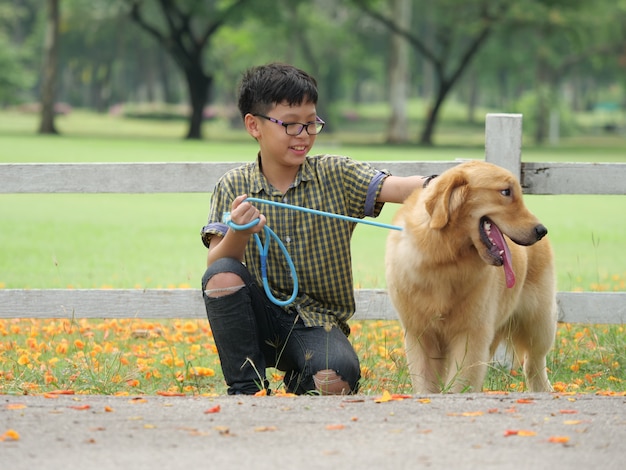 Азиатский мальчик играет с щенком собака золотой retreiver в парке