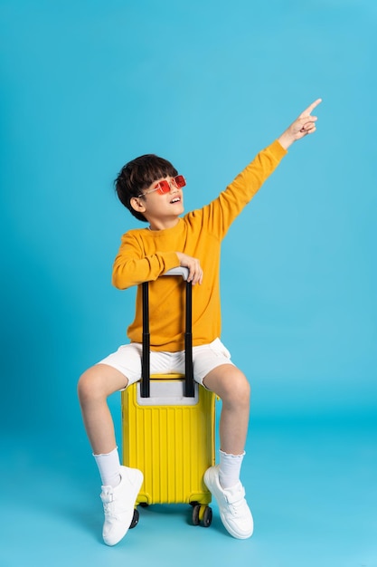 青の背景にスーツケースを引っ張るアジアの少年