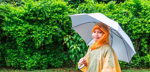 写真 アジアの少年はレインコートを着て、雨の日に傘を開きます