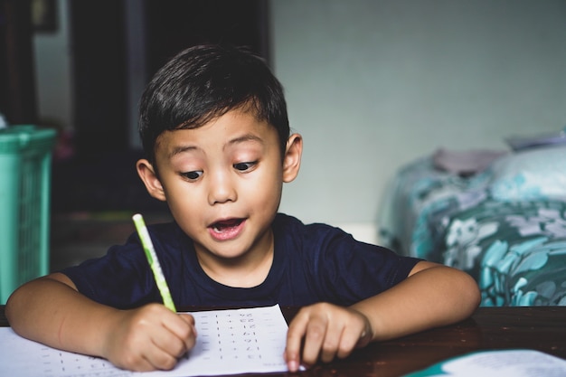 机の後ろに座っているアジア人の少年が興奮した表情で何かを書いていた