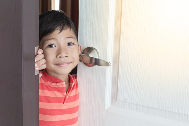 笑みを浮かべて、アジアの少年が自宅で白いドアを開けた