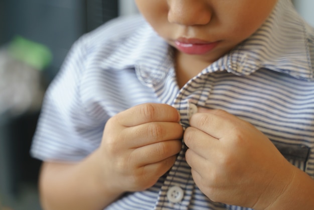 Asian boy trying to buttoning his shirt by himself