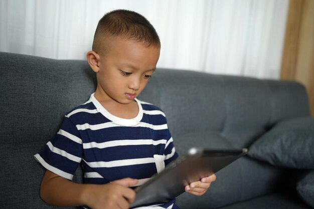 Asian boy uses tablet to watch video clips on sofa in home