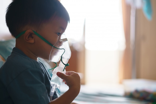 Asian boy using inhaler containing medicine to stop coughing